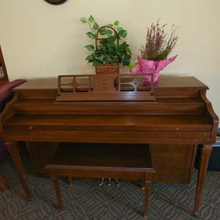 A wooden piano with a matching bench, decorated with plants and flowers on top.