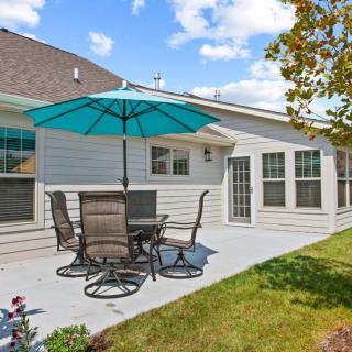 A cozy backyard patio with table, chairs, and a large umbrella under a clear blue sky.