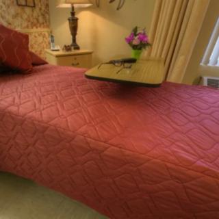 A cozy bedroom setup with a quilted bedspread, a side lamp, and flowers on a bedside table.