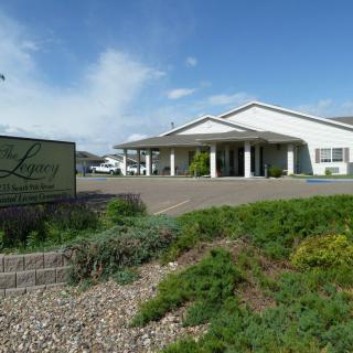 A large white building with a sign in front, surrounded by greenery under a clear blue sky.
