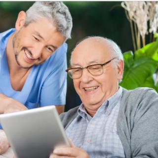 An elderly man and a younger man smiling while looking at a tablet together.