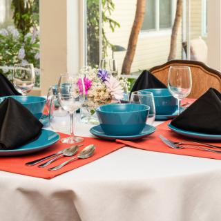 A beautifully set dining table with turquoise dinnerware, black napkins, and a floral centerpiece.