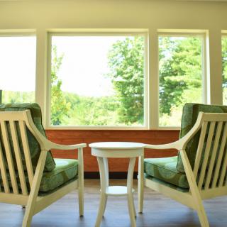 A peaceful sitting area with two chairs and a table overlooking lush greenery through large windows.