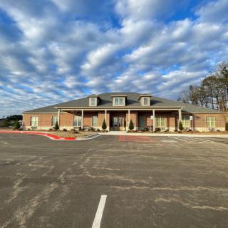 A view of a building with a cloudy sky in the background and an empty parking lot in the foreground.