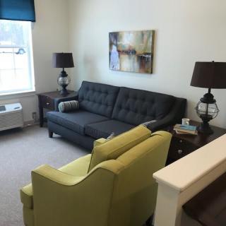 A cozy living room with a dark sofa, bright armchairs, and decorative lamps.