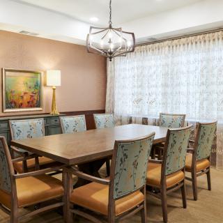 A formal dining room with a wooden table and chairs, featuring a chandelier and wall art.
