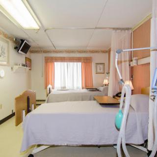 A view of a hospital patient room with two beds and natural light coming through the window.