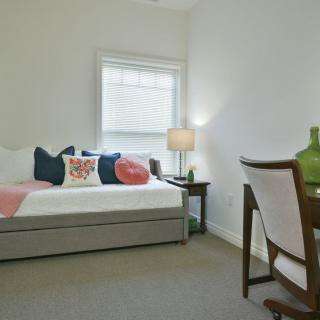 A minimalist bedroom with a daybed, decorative pillows, a desk, and a lamp.