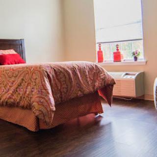 A cozy bedroom featuring a neatly made bed, wooden flooring, and vibrant decorative elements.