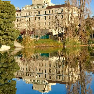 A large building reflected in a calm lake amidst surrounding trees.