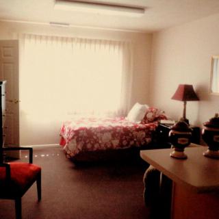 A cozy bedroom with a bed, lamp, and chair near a window.