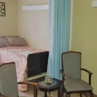 A cozy bedroom with a bed, two chairs, and a small table separated by a curtain.