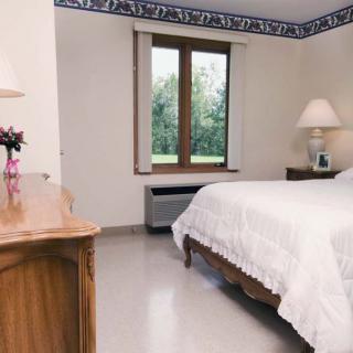 A cozy bedroom with a white bedspread, wooden furniture, and natural light from the window.