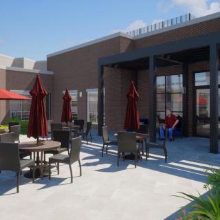 A modern outdoor patio area with tables, chairs, and red umbrellas next to a building.