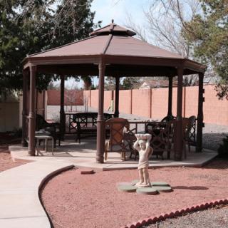 A wooden gazebo in a backyard setting, surrounded by trees and landscaped paths.