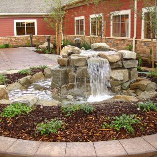 A small garden waterfall surrounded by stones and plants in a landscaped area.