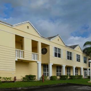 A view of a yellow residential apartment complex with balconies and a palm tree nearby.