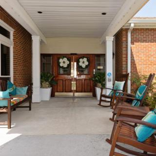 A welcoming porch entrance with rocking chairs and decorative pillows, adorned with potted plants.