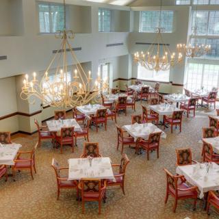 A spacious and elegant dining area with chandeliers, featuring neatly arranged tables and chairs in a well-lit setting.