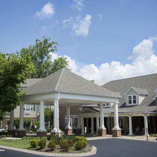 A residential building with a covered entrance and surrounding trees under a partly cloudy sky.