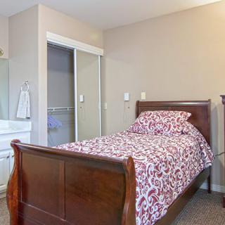 A cozy bedroom with a single wooden bed, patterned bedding, and an adjacent closet with mirrored sliding doors.