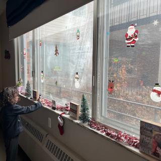 A child admires the festive Christmas decorations displayed on a window, filled with snowmen and Santa Claus figures.