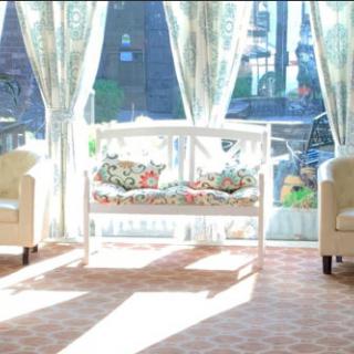 A sunlit room with two chairs, a decorative bench, and large windows with sheer curtains.