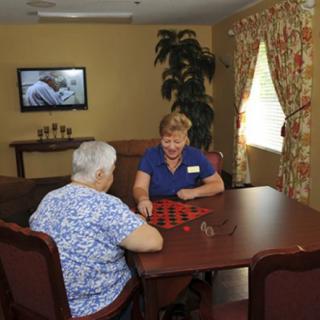 An elderly woman and a caregiver playing checkers in a cozy room.
