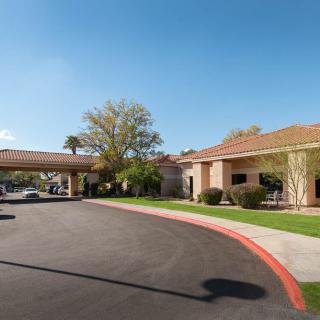 A sunny day view of a building with a driveway and landscaped surroundings.