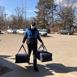 A delivery person carrying two large bags on a sunny day.