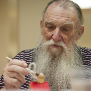 An elderly man with a long beard using chopsticks to eat.