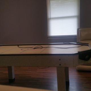 An indoor air hockey table in a recreation room with a window and seating nearby.