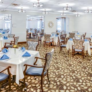 An elegant dining room with neatly arranged tables and chairs, featuring white tablecloths and blue napkins.