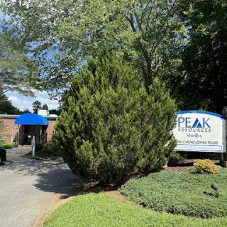 Entrance to Peak facility with lush greenery and a welcoming sign.