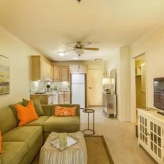 A modern open-plan living room and kitchen with a green sofa, orange cushions, and a television.