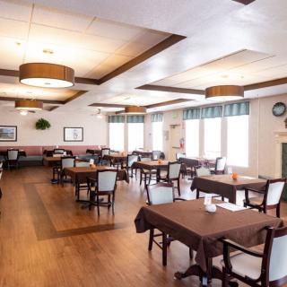 An empty dining room with neatly arranged tables and chairs, featuring wooden floors and modern light fixtures.