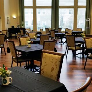 An empty dining room with neatly arranged tables and chairs, featuring large windows and a wooden floor.