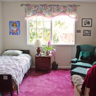 A cozy bedroom with a single bed, an armchair, and a window bringing in natural light.