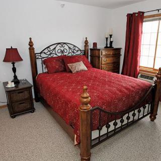 A cozy bedroom with a red bedspread and decorative wooden furniture.