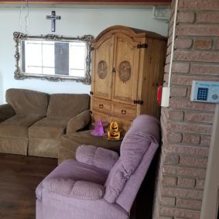 A cozy living room featuring a purple chair, a beige sofa, a wooden cabinet, and decorative elements.
