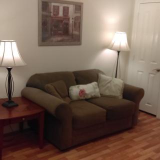 A cozy living room with a brown sofa, two standing lamps, and a painting on the wall.