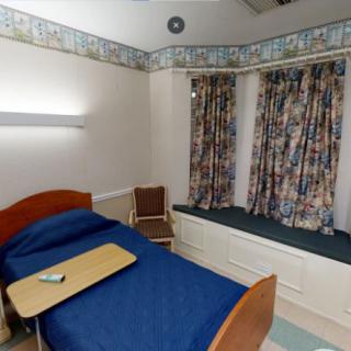 A hospital room with a single bed, curtains, and basic furnishings.