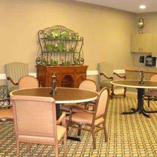 A cozy dining area with round tables and padded chairs, featuring a patterned carpet and decorative shelving.