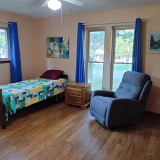 A cozy bedroom featuring a bed, recliner, and large windows allowing natural light.