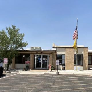 A small building with a flagpole displaying the American flag, situated in a parking lot under a clear blue sky.