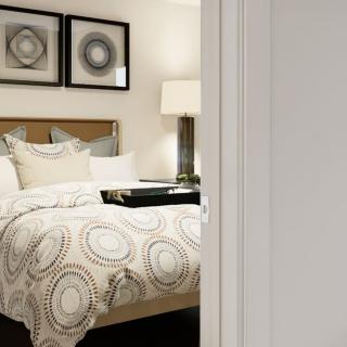 A cozy bedroom featuring a neatly made bed with patterned bedding, artwork on the wall, and a stylish lamp.