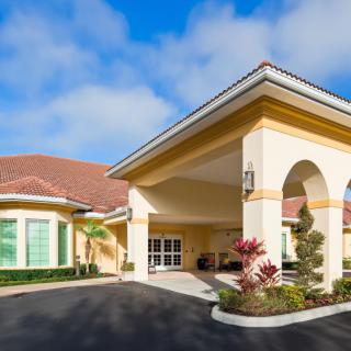 A bright and welcoming building entrance with landscaped surroundings under a blue sky.