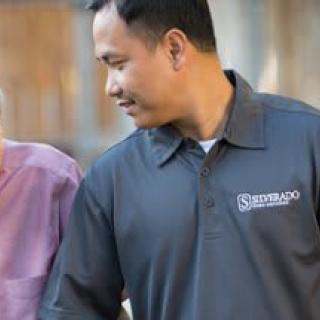 A caregiver providing support to an elderly person outdoors.