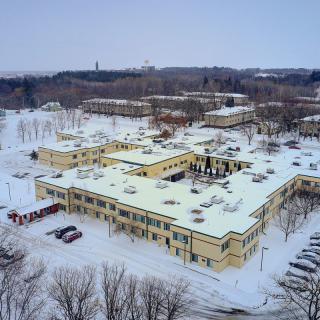 Aerial view of snow-covered buildings surrounded by trees in a winter landscape.