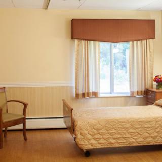 A minimalist bedroom with a single bed, wooden chair, and a window with curtains.